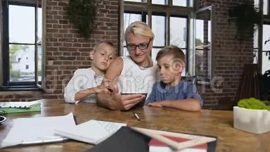 戴眼镜的白人中年妇女在平板电脑上做两个小学生的运动，和奶奶一起玩的快乐小男孩